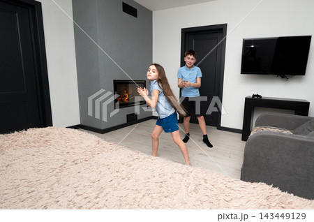 Children engage in playful dance in modern living room during playful afternoon at home, creating joyful memories through movement and laughter Children engage in playful dance in modern living room during playful afternoon at home, creating joyful memories through movement and laughter 143449129
