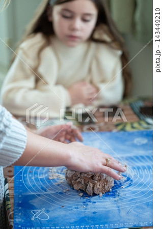 A child watches as an adult kneads dark-colored dough on a blue mat. A child watches as an adult kneads dark-colored dough on a blue mat. 143449210