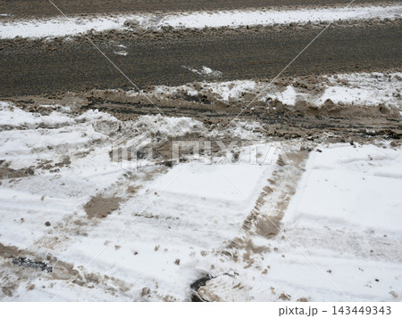 Snow-covered road surface with dirty slush, tire tracks and exposed asphalt after winter traffic. 143449343
