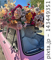Pink vintage car topped with abundant colorful flowers and giant teddy bear in passenger seat for romantic display and floral banner 143449351