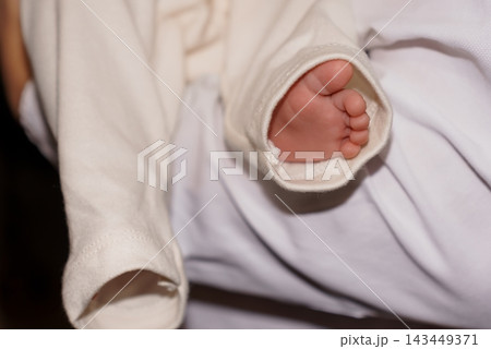 Tiny newborn foot peeking out from white clothing sleeve resting on soft fabric bedding background Tiny newborn foot peeking out from white clothing sleeve resting on soft fabric bedding background 143449371