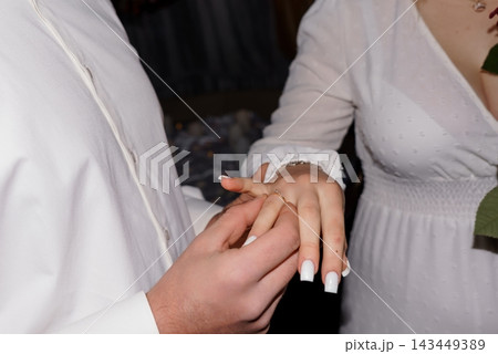 Groom placing diamond wedding ring on bride finger in white attire Groom placing diamond wedding ring on bride finger in white attire 143449389