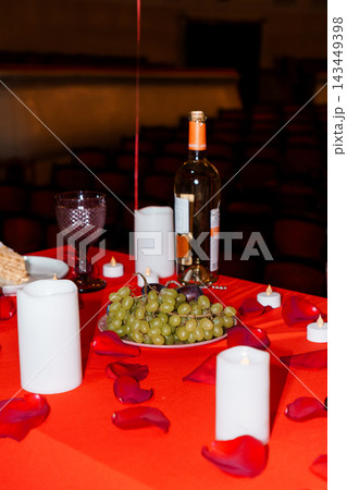 Romantic wine table setting with green grapes and red rose petals in candlelight theater environment 143449398