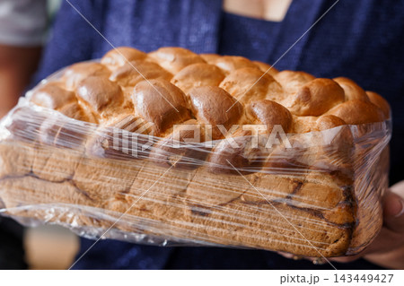 Woman holding large loaf of plastic wrapped sweet braided bread with golden brown crust and textured pattern Woman holding large loaf of plastic wrapped sweet braided bread with golden brown crust and textured pattern 143449427