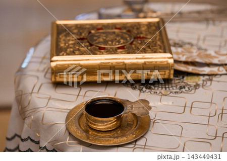 Gold Qur'an box and traditional tea glass on embroidered white cloth with Islamic cultural context. Gold Qur'an box and traditional tea glass on embroidered white cloth with Islamic cultural context. 143449431