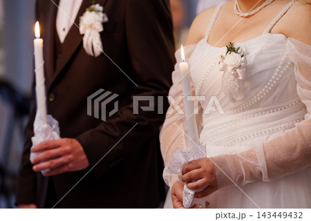 Bride and groom in white dress and brown suit holding burning candles at a wedding ceremony Bride and groom in white dress and brown suit holding burning candles at a wedding ceremony 143449432