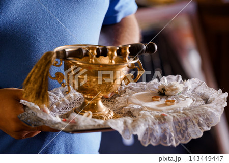 Man in blue shirt holding ornate brass chafing dish with gold wedding rings on lace tray for ceremony service Man in blue shirt holding ornate brass chafing dish with gold wedding rings on lace tray for ceremony service 143449447