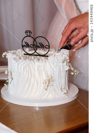 Couple cutting white wedding cake with ring topper on wooden table 143449468