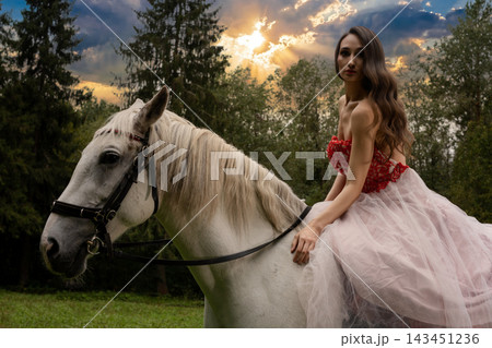 Woman in a red lace and tulle dress seated on a white horse Woman in a red lace and tulle dress seated on a white horse 143451236