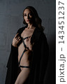 Woman in black leather harness and coat against dark concrete wall, dramatic studio lighting with moody atmosphere 143451237