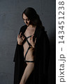 Woman in black leather harness and open coat against dark textured wall, dramatic side lighting, moody atmosphere 143451238