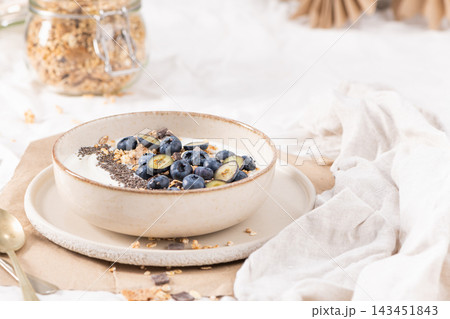 Fresh yogurt bowl topped with ripe blueberries and crunchy granola served in a ceramic dish on a light kitchen setting for a nutritious meal 143451843