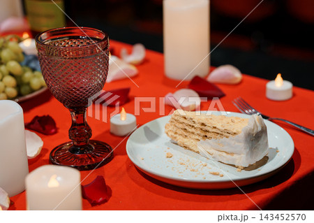 Romantic dessert table with wine glass slice of cake rose petals red cloth candlelight Romantic dessert table with wine glass slice of cake rose petals red cloth candlelight 143452570