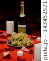 Green grapes on a plate with wine bottle and tealights on red tablecloth featuring scattered rose petals in romantic setting 143452571