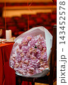Large bouquet of dried pink roses wrapped in white paper resting on a theater chair with red background 143452578