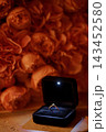 Gold diamond ring in open black velvet box surrounded by warm blurred orange roses for romantic proposal context 143452580