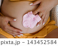 Pregnant belly with pink baby socks in hands showing gender reveal close up shot in warm yellow tones 143452584
