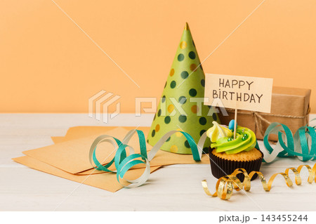 Delicious cupcake, gift and dotted cap on yellow background, copy space. Birthday, party, holiday concept Delicious cupcake, gift and dotted cap on yellow background, copy space. Birthday, party, holiday concept 143455244