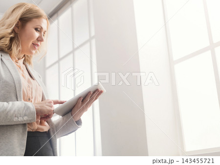 Happy businesswoman at work using digital tablet while standing near window at modern office, copy space 143455721
