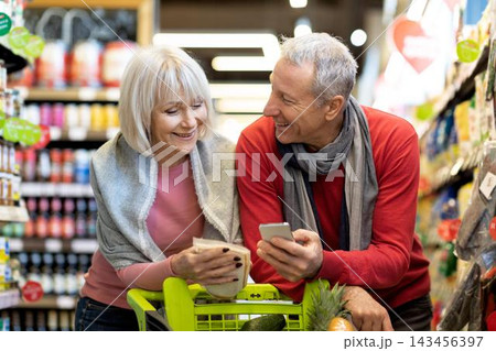 Happy Elderly Couple, Caucasian Man And Woman, Smiling And Choosing Fresh Produce Together In Supermarket, Enjoying Their Shopping Experience. Weight Loss Concept. 143456397