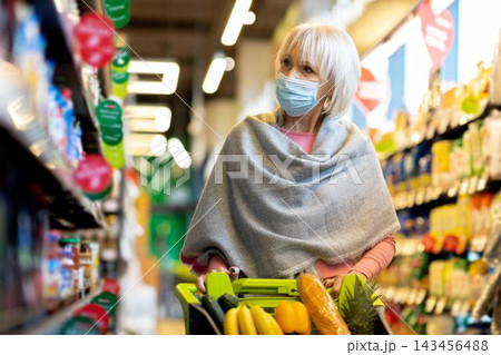 Focused Senior Caucasian Woman Wearing Mask While Shopping For Fresh Fruits And Vegetables In Grocery Store, Standing Next To Shelves Filled With Products. Healthy Lifestyle Concept. 143456488
