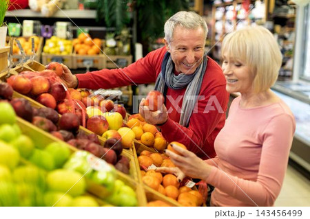 Smiling Elderly Caucasian Man And Woman Shopping Together In Supermarket, Choosing Fresh Organic Fruits, Enjoying Their Time While Holding Fruits At Store. Positive Senior Couple Moment. Smiling Elderly Caucasian Man And Woman Shopping Together In Supermarket, Choosing Fresh Organic Fruits, Enjoying Their Time While Holding Fruits At Store. Positive Senior Couple Moment. 143456499