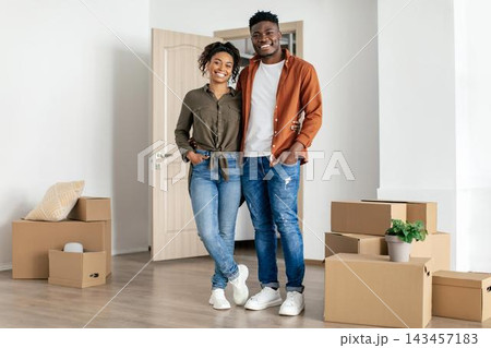 Smiling Young African American Couple Standing Together In New Apartment Amongst Moving Boxes, Displaying Emotion Of Happiness, Feeling Excited About Moving In Together. Home Concept. Smiling Young African American Couple Standing Together In New Apartment Amongst Moving Boxes, Displaying Emotion Of Happiness, Feeling Excited About Moving In Together. Home Concept. 143457183
