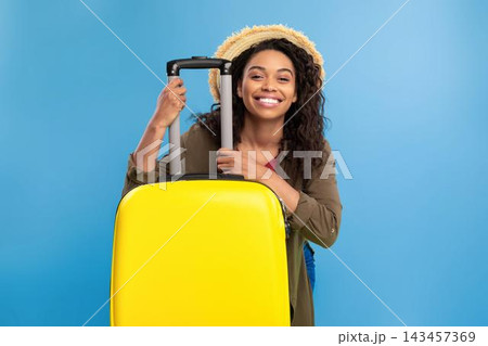 Happy Smiling Black Woman Holding Yellow Luggage, Excitedly Preparing For Trip, Standing Indoors With Blue Background, Ready For Adventure, Travel Concept. Happy Smiling Black Woman Holding Yellow Luggage, Excitedly Preparing For Trip, Standing Indoors With Blue Background, Ready For Adventure, Travel Concept. 143457369