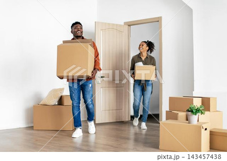 Smiling Black Couple Moving Into New Home, Carrying Boxes And Enjoying Their Time Together. Young Adults Bringing Belongings Into Living Room, Light And Bright Space, Home And Family Concept. 143457438