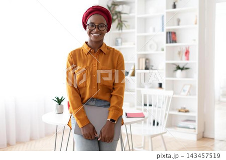 Smiling Black Woman In Casual Attire Holding Laptop While Standing In Home Office, Creating Positive Work Environment. Confident Professional Making Plans Or Preparing For Meeting, Business Concept. Smiling Black Woman In Casual Attire Holding Laptop While Standing In Home Office, Creating Positive Work Environment. Confident Professional Making Plans Or Preparing For Meeting, Business Concept. 143457519