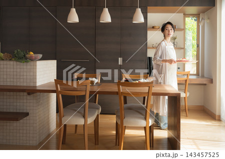 一戸建てのキッチンとダイニングで料理を運ぶ日本人女性、新築住宅のマイホームで家事など理想のイメージ 一戸建てのキッチンとダイニングで料理を運ぶ日本人女性、新築住宅のマイホームで家事など理想のイメージ 143457525