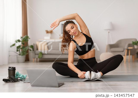 Focused Young Woman Stretching While Sitting On Yoga Mat At Home, Engaging In Exercise Routine For Fitness And Wellness In Modern Living Room Setting. Weight Loss Concept. Focused Young Woman Stretching While Sitting On Yoga Mat At Home, Engaging In Exercise Routine For Fitness And Wellness In Modern Living Room Setting. Weight Loss Concept. 143457547