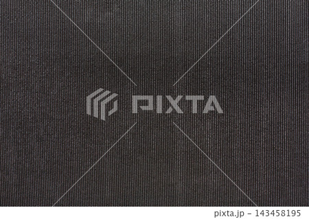 A black patterned fabric is shown up close. The texture is visible with a fine grid design. The lighting reveals details of the material. This setting is simple with focus on the fabric texture. 143458195