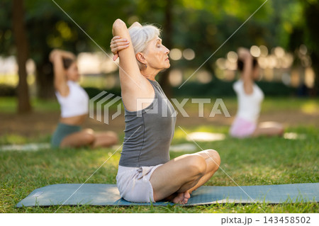 Elderly woman stretching in lotus position at outdoor yoga class Elderly woman stretching in lotus position at outdoor yoga class 143458502