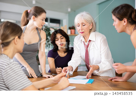 Mature woman standing and leading a group discussion with diverse ladies Mature woman standing and leading a group discussion with diverse ladies 143458535