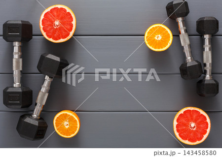 Two sets of black dumbbells rest on a gray table along with fresh grapefruit and orange slices. This scene emphasizes a connection between fitness and healthy eating. Two sets of black dumbbells rest on a gray table along with fresh grapefruit and orange slices. This scene emphasizes a connection between fitness and healthy eating. 143458580