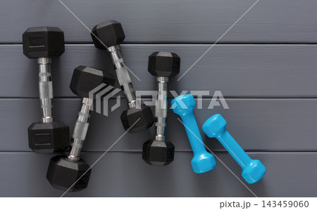 A set of black and blue dumbbells lay on a gray surface. The dumbbells are placed randomly, indicating a recent workout. The environment suggests an indoor gym area. A set of black and blue dumbbells lay on a gray surface. The dumbbells are placed randomly, indicating a recent workout. The environment suggests an indoor gym area. 143459060