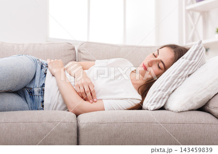 A woman lies on a light sofa taking a rest. She has her arms relaxed and eyes closed. The room is bright with natural light coming through the window. This moment captures a time of relaxation. A woman lies on a light sofa taking a rest. She has her arms relaxed and eyes closed. The room is bright with natural light coming through the window. This moment captures a time of relaxation. 143459839