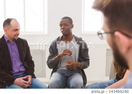 A group of men and women sit in a circle in a bright room. One person speaks, sharing thoughts while others listen attentively. The atmosphere shows engagement and connection among participants. A group of men and women sit in a circle in a bright room. One person speaks, sharing thoughts while others listen attentively. The atmosphere shows engagement and connection among participants. 143460280