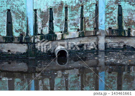 Industrial concrete drainage pipe protruding over stagnant dirty canal water with floating garbage debris. 143461661