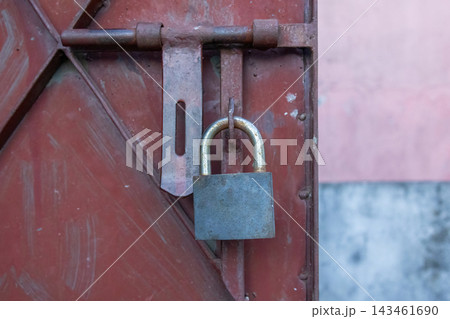 Heavy metal padlock locking rusted iron door latch outdoors in daylight. Security protection system for residential entrance gate. Heavy metal padlock locking rusted iron door latch outdoors in daylight. Security protection system for residential entrance gate. 143461690