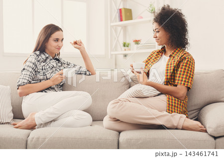 Two friends sit on a couch in a bright room, sharing coffee and conversation. They wear casual clothing and show smiles, creating a relaxed atmosphere in the afternoon sun. Two friends sit on a couch in a bright room, sharing coffee and conversation. They wear casual clothing and show smiles, creating a relaxed atmosphere in the afternoon sun. 143461741