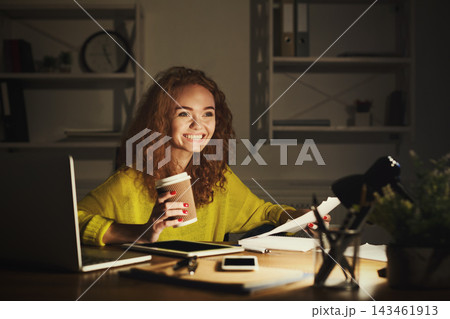 A woman sits at a desk working late at night. She holds a coffee cup while smiling. A laptop and papers are in front of her. Books and a lamp are present in a simple setting. A woman sits at a desk working late at night. She holds a coffee cup while smiling. A laptop and papers are in front of her. Books and a lamp are present in a simple setting. 143461913