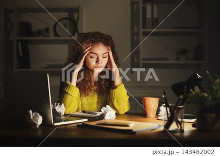 A young woman sits at a desk in a dimly lit room. She is focused and stressed as she works on her collage. There are crumpled papers around her, and a laptop is open next to her. A young woman sits at a desk in a dimly lit room. She is focused and stressed as she works on her collage. There are crumpled papers around her, and a laptop is open next to her. 143462002