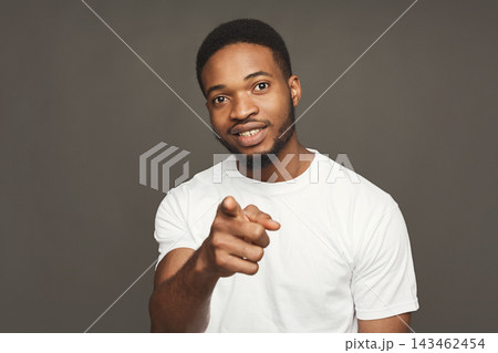 A man stands indoors with a neutral background, pointing directly at the viewer. He wears a plain white shirt and smiles. His expression shows confidence and approachability during the moment. A man stands indoors with a neutral background, pointing directly at the viewer. He wears a plain white shirt and smiles. His expression shows confidence and approachability during the moment. 143462454