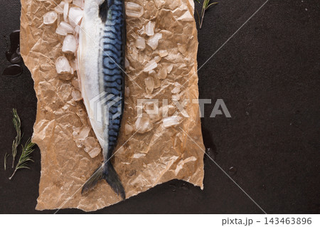 A mackerel fish lies on a brown paper with ice around it. This scene shows the fish laid out in a kitchen. The setting is prepared for cooking or meal preparation. A mackerel fish lies on a brown paper with ice around it. This scene shows the fish laid out in a kitchen. The setting is prepared for cooking or meal preparation. 143463896