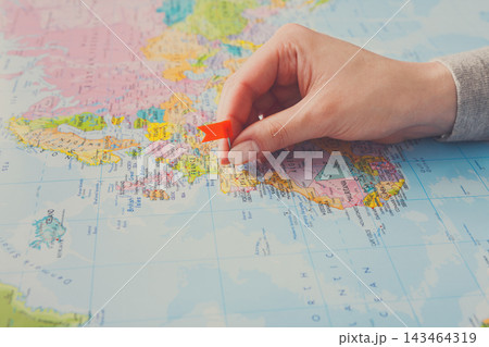 A person marks a specific spot on a world map using a red marker. This activity takes place in a bright room during a travel planning session. Maps and exploration are the focus. 143464319