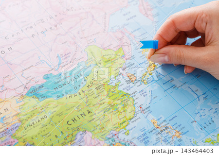 A hand holds a blue flag pointing to a spot on a map of Asia. The map shows several countries with clear borders. The activity seems focused on finding or marking a specific place. A hand holds a blue flag pointing to a spot on a map of Asia. The map shows several countries with clear borders. The activity seems focused on finding or marking a specific place. 143464403