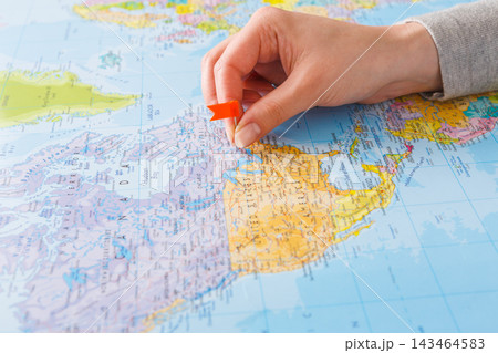 A hand is positioning a red push pin on a map of North America. The map shows detailed geographic features and various locations. This action indicates finding or marking an important place. 143464583