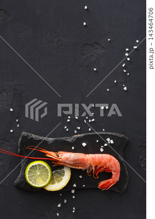 Fresh shrimp is placed on a black stone plate alongside slices of lemon. White salt is scattered around the dish. This setup is in a kitchen with a simple and clean style. Fresh shrimp is placed on a black stone plate alongside slices of lemon. White salt is scattered around the dish. This setup is in a kitchen with a simple and clean style. 143464706